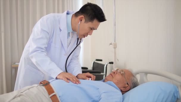 アジア系男性医師は 聴診器を使って 病気で病床にあるアジア系の老人の肺や心臓の音を聞きます 高齢者の医療支援 Conep — ストック動画