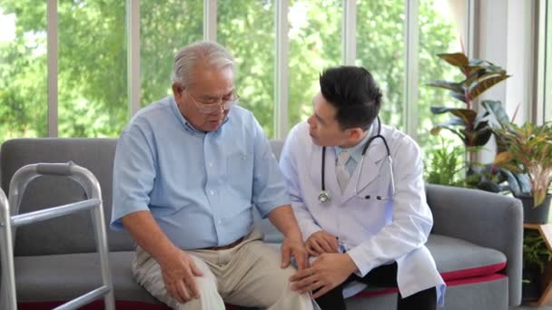 Азиатский Врач Мужчина Белом Халате Проверяет Колено Пожилого Пациента Сидящего — стоковое видео