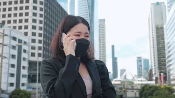都市部の電話で顔のマスクをしたアジアのビジネス女性 携帯電話を使用して電話の呼び出しを聞く若いビジネス女性 — ストック動画