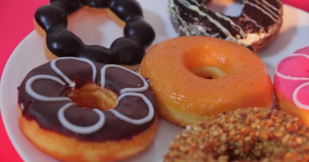 Вкусные Сладкие Пончики Разных Цветов Белой Тарелке Красным Фоном — стоковое видео