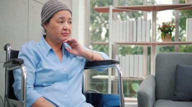 Yaşlı, yaşlı Asyalı büyükanne, tekerlekli sandalyede oturmuş pencereden dışarı bakıyor ve düşünüyor. Yalnız, yaşlı bir kadın evde tek başına bir gün geçiriyor. Aile hayat sigortası kavramı.