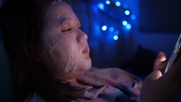 Азійка Дістає Маску Обличчі Лежачи Ліжку Дивиться Товари Онлайновому Одязі — стокове відео