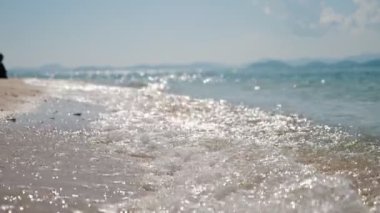 Turkuaz su ve sarı kumla güzel, temiz bir kumsalın ağır çekimleri. Deniz kıyısındaki dalgalar, yaz mevsimi arka planı, güzel deniz manzarası.