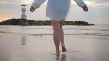 Beyaz elbiseli genç bir kadın gün batımında sahilde tek başına yürüyor..