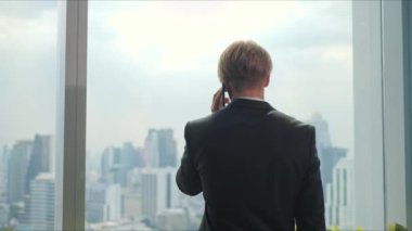 Genç bir işadamı ayakta duruyor ve telefonda konuşuyor. Kendini işine adamış..