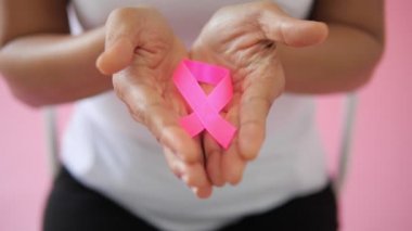 Hand 'in pembe arka planda pembe kurdeleyle kameraya yakın çekim. Dünya göğüs kanseri günü konsepti. Göğüs kanseri sembolü.
