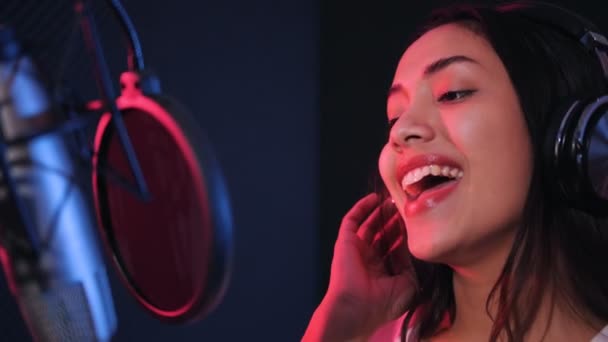 专业精力充沛的亚洲混音女歌手头戴耳机 一边在背景音乐工作室录制 一边用麦克风演唱一首新歌 — 图库视频影像
