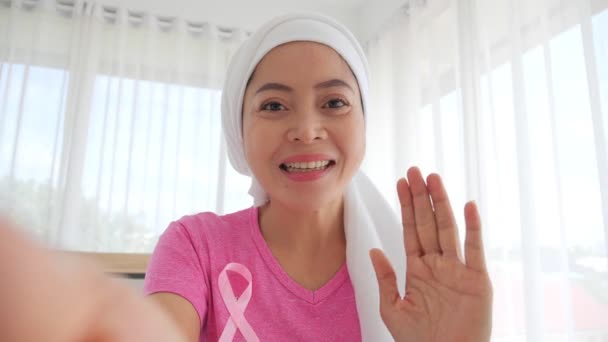 若い大人のアジアの女性癌患者ピンクの乳癌意識リボンとスカーフを身に着けている患者笑顔とカメラの応援で話してサポートは乳癌患者に共感を与える — ストック動画