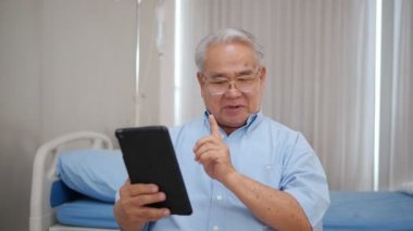 Mutlu Asyalı yaşlı adam elinde tablet tutarak video izliyor internetten arıyor. Ekrana bakıyor, hastaneye gülümsüyor. Büyükbabaları modern teknoloji aletini kullanarak öğreniyor..