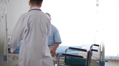 Asyalı doktor, tekerlekli sandalyede oturan engelli yaşlı hastaya, doktor bakıcıya veya hemşireye yardım eder. Gülümseyen yaşlı engelli büyükbabaya, yaşlı sağlık hizmetleri konseptine yardımcı olur.