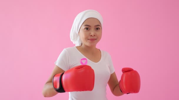 亚洲女人 带着粉红缎带和拳击手套 在粉红的背景上看着相机 乳腺癌概念 — 图库视频影像