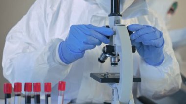 Biyolojik tehlike koruma giysileri içinde Asyalı doktor laboratuarda mikroskop ve aşı araştırmalarında virüs örneğini analiz ediyor. Karantina veya virüs salgını kavramı.