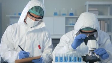 Biyolojik tehlike koruma giysisinde Asyalı doktor bilim adamı laboratuarda mikroskop ile covid 19 numunesini inceliyor. Coronavirus covid 19 aşı araştırması. Karantina veya virüs salgını kavramı. 