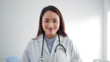 Beyaz önlüklü, omuzlarına steteskop takmış, gülümseyen genç Asyalı kadın doktor portresi..
