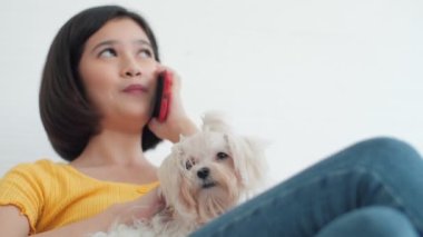 Asyalı genç bir kadın evde köpeğini okşarken telefonda konuşuyor..