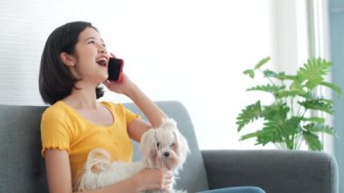 Asyalı genç bir kadın evde köpeğini okşarken telefonda konuşuyor..