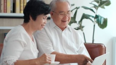 Mutlu Asyalı yaşlı çift dizüstü bilgisayarlarını kullanarak internetten alışveriş yapıyor, yetişkin bir ailenin internet haberlerini okuyor, internet haberlerini tartışıyor, internet sitesinden seyahat teklifini seçiyor..