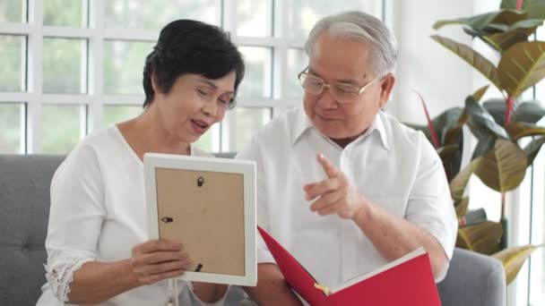 Glückliches Asiatisches Seniorenpaar Beim Betrachten Des Familienfotobuchs Auf Dem Heimischen — Stockvideo