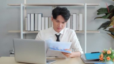 Asyalı işadamı ofis çalışanı koltuğunda oturup mutsuz hissederek kağıtları fırlatıyor. İnsanlar ve sorunlar kavramı.
