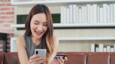 Kredi kartı ve akıllı telefon taşıyan Asyalı kadın müşteriler kanepe alışverişinde oturuyorlar ve çevrimiçi dükkanlardan hızlı ve kolay cep telefonu ödemeleri yapıyorlar. E-bankacılık uygulama servisi.