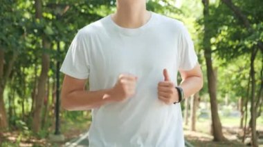 Sport Asian man running in park on public green background, Fit man jogging at outdoor workout on background of trees. Healthy lifestyle concept. Slow motion