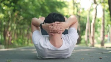 Back view of Strong young man doing sit-up exercise on road at outdoor green park.