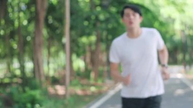 Sportif Asyalı genç adam koşuyor ve nefes almak için eğiliyor..