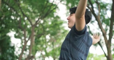Happy Asian handsome man breathing deep fresh air in the park with trees in the background. Stop and smell the tree, connect with nature.