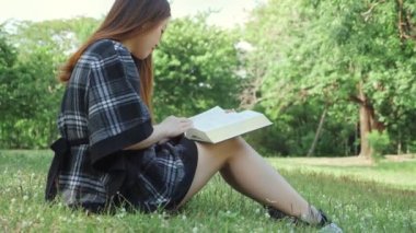 Kadın yeşil parkta kitap okuyarak rahatlıyor, öğrenci onların bilgisini, rahatlığını, etkinliğini ve yaşam tarzını geliştirmek için kitabı okuyor..