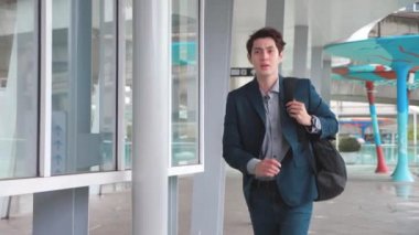 Genç işadamının yavaş çekim 4K 'sı koşar ve kendine güvenen adamın buluşmaya ve çalışmaya geç kalmasına bakar. Takım elbiseli bir adam modern binanın yakınında koşuyor. Randevu için acele eden yakışıklı adam..