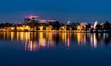 Herastrau parkından gölün suyundaki şehir ışıklarının renkli yansımasının gece görüşü. Bükreş, Romanya.
