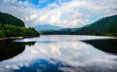 Dağların arasındaki güzel Oasa Gölü bulutları ve gökyüzünü yansıtıyor, Transalpina Yolu, Romanya