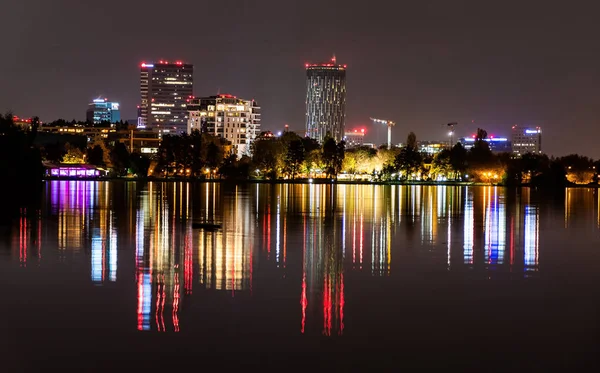 BUCHAREST, ROMANIA - 30 Ekim 2021 Herastrau Parkı 'ndan gölün suyundaki şehir ışıklarının renkli yansımasının gece görüntüsü. 