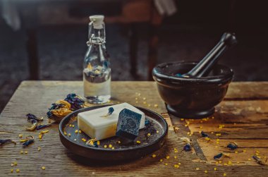 Masanın üzerine yerleştirilmiş bir fotoğraf. El yapımı sabun, kuru çiçekler, dekor. Kahverengi ahşap arka plan, boyalı cam işçiliği 
