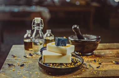 Masanın üzerine yerleştirilmiş bir fotoğraf. El yapımı sabun, kuru çiçekler, dekor. Kahverengi ahşap arka plan, boyalı cam işçiliği 