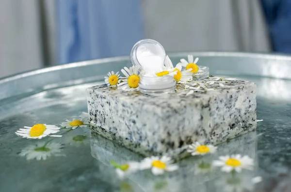 ハンドメイド化粧品 90度の角度でテーブルの上に撮影する 水のテーブルにバターと香水のボトル 新鮮なカモミールの花の周りにクリームの花崗岩の石で — ストック写真