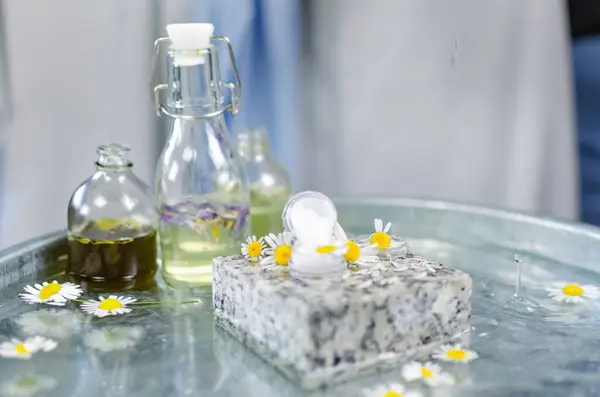 Handmade cosmetics. Shooting on the table at an angle of 90 degrees. Bottles of butter and perfume on a table of water. On a granite stone can of cream, around fresh chamomile flowers