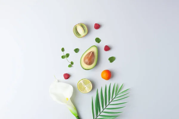 Summer fruit composition. Creative tropical background made from fresh fruits and palm leaves on grey. Flat lay, copy space.