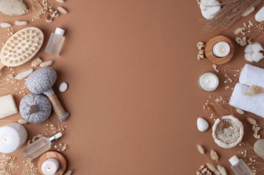 Kozmetik şişeli, mumlu ve bitkisel çantalı spa tedavisi, kahverengi arka planda havlu. Düz yat, boşluğu kopyala.