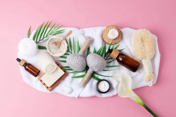 Spa treatment with natural skin care products, candles and herbal bag, towel on pink background. Flat lay.