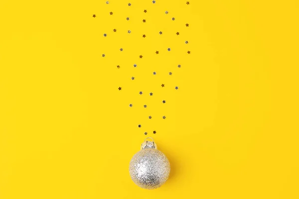 Christmas yellow minimal background with grey ball and confetti. Flat lay, copy space
