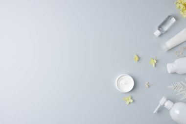 Gri arka planda çiçekleri olan kozmetik cilt bakım ürünleri. Düz yat, boşluğu kopyala