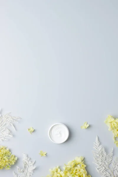 Jar of cosmetic cream with flowers on grey background. Flat lay, copy space
