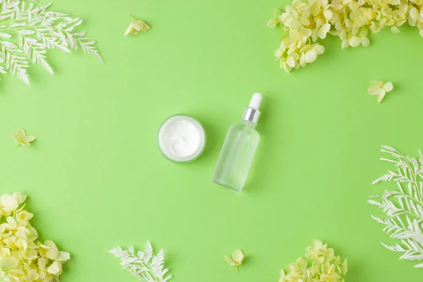 Cosmetic skin care products with flowers on green background. Flat lay