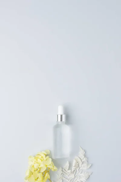 Cosmetic bottle with flowers on grey background. Flat lay, copy space