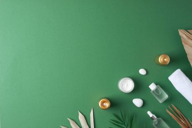 Yeşil arka planda kozmetik şişeli, mumlu ve palmiye yapraklı spa tedavisi. Düz yat, boşluğu kopyala