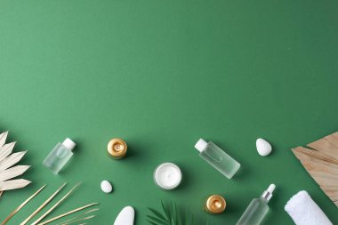 Yeşil arka planda kozmetik şişeli, mumlu ve palmiye yapraklı spa tedavisi. Düz yat, boşluğu kopyala