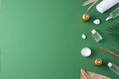 Yeşil arka planda kozmetik şişeli, mumlu ve palmiye yapraklı spa tedavisi. Düz yat, boşluğu kopyala
