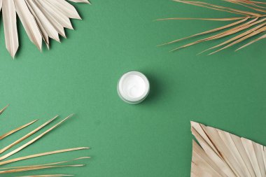 Yeşil arka planda palmiye yaprağı olan bir kavanoz kozmetik kremi. Düz yatıyordu