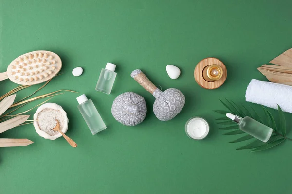 Spa treatment with natural skin care products, herbal bag, towel and palm leaf on green background. Flat lay, copy space.